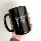 A hand holding a glossy black ceramic mug with the phrase 'CREATIVITY WITHOUT LIMITS' printed in white capital letters on the front, set against a solid white background