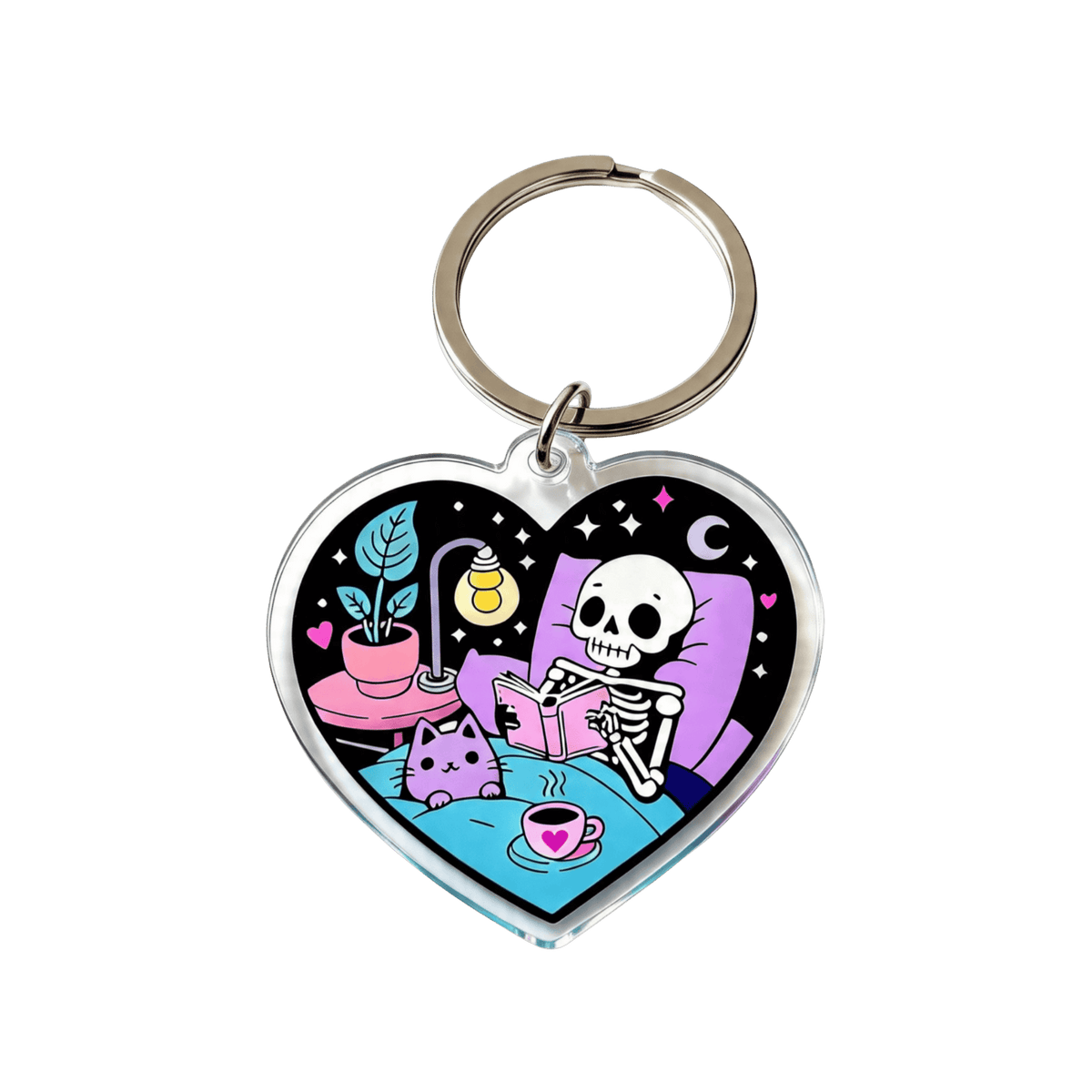 A colorful heart-shaped acrylic keychain featuring a skeleton reading a book, a cat, and a coffee mug resting on a bed with a split ring clip on a white background