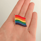 A hand holding a rainbow flag pin on a white background