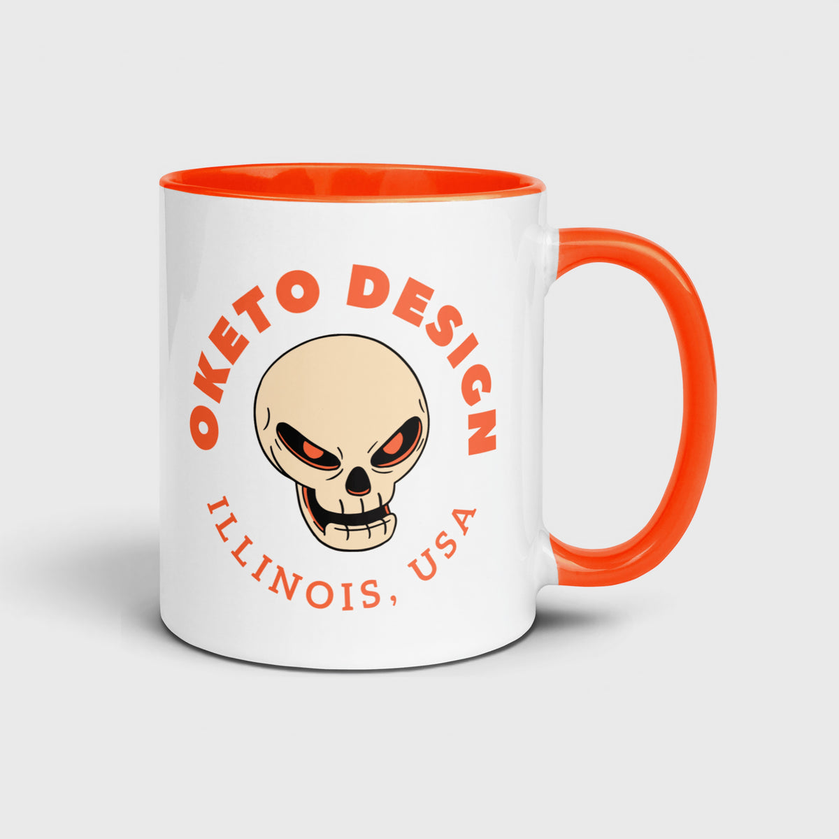 White Oketo Design coffee mug with an orange handle and interior, featuring an orange skull logo