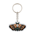 An acrylic keychain featuring a stylized moth with orange, black, and teal patterns, a white skull at the center, and a silver metal key ring and chain