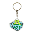 A clear acrylic keychain charm shaped like a light blue teacup with green leaf patterns, featuring a cute green frog sitting in the center, attached to a chain and a split key ring on a white background